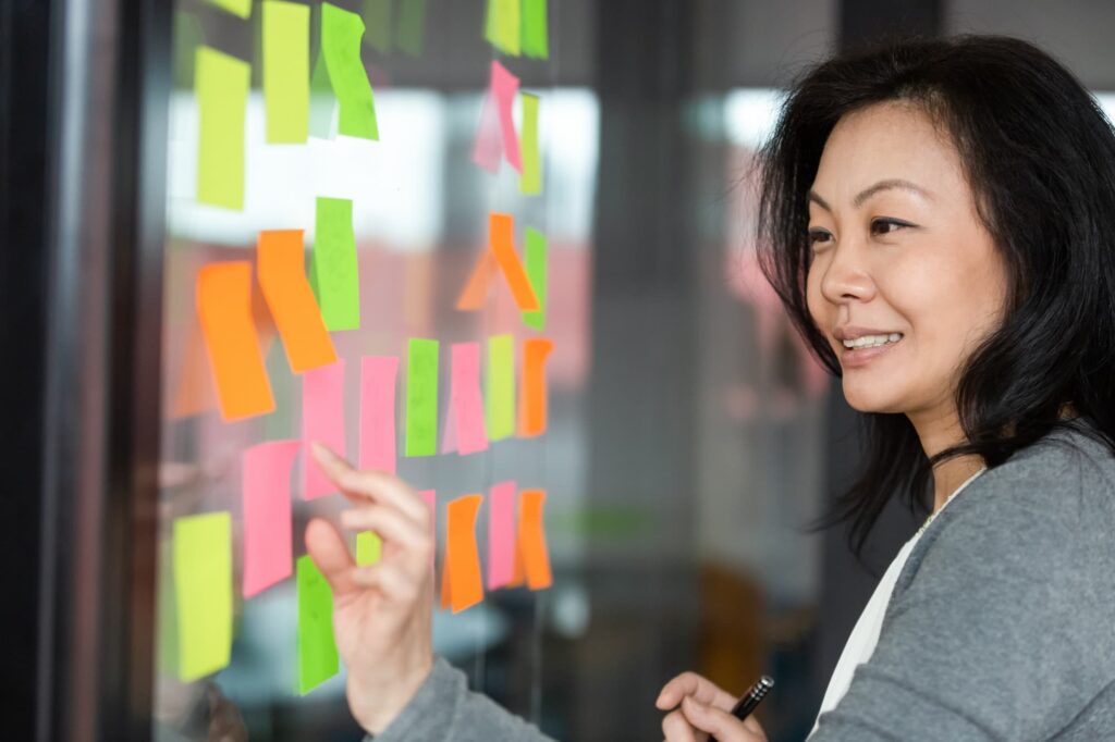 Data strategy and insights - Person organising colourful sticky notes on a glass wall.

