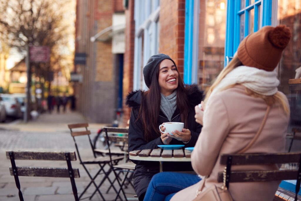 Consumer spend data - Two people sitting at an outdoor cafe table, each holding a cup