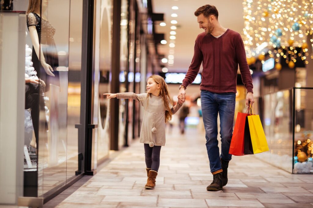 Real estate insights - A man and young girl walking in a mall. Young girl is pointing at a store window.