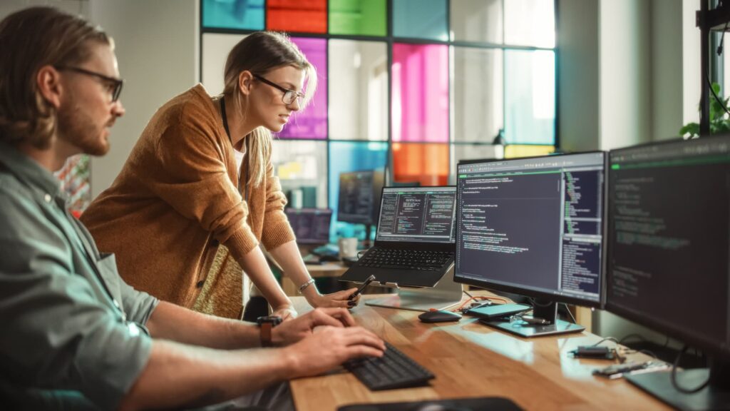 Architecting for AI - A man and women working at a desk with multiple monitors showing code.