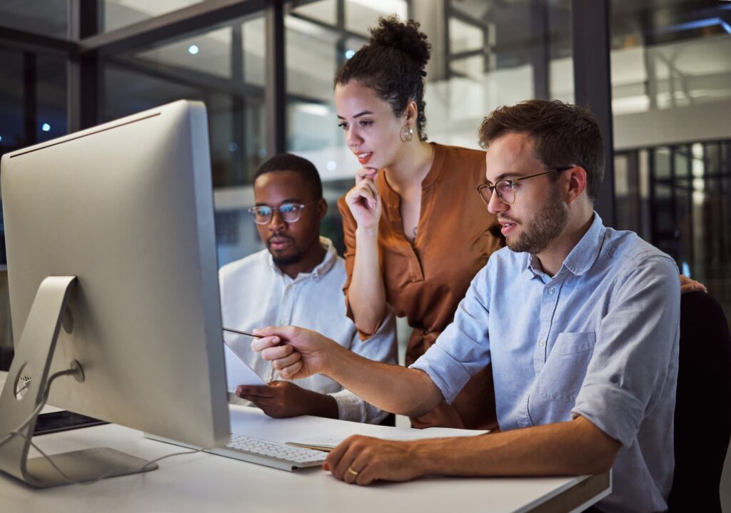 Creative design and technology - Two men and one women in an office collaborate around a computer, with one pointing at the screen.

