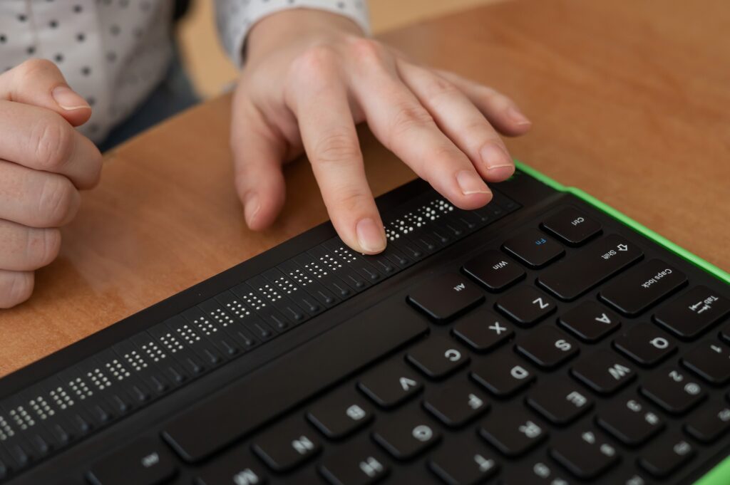Digital accessibility - A person using a Braille display keyboard with fingers on the Braille section above the standard keys